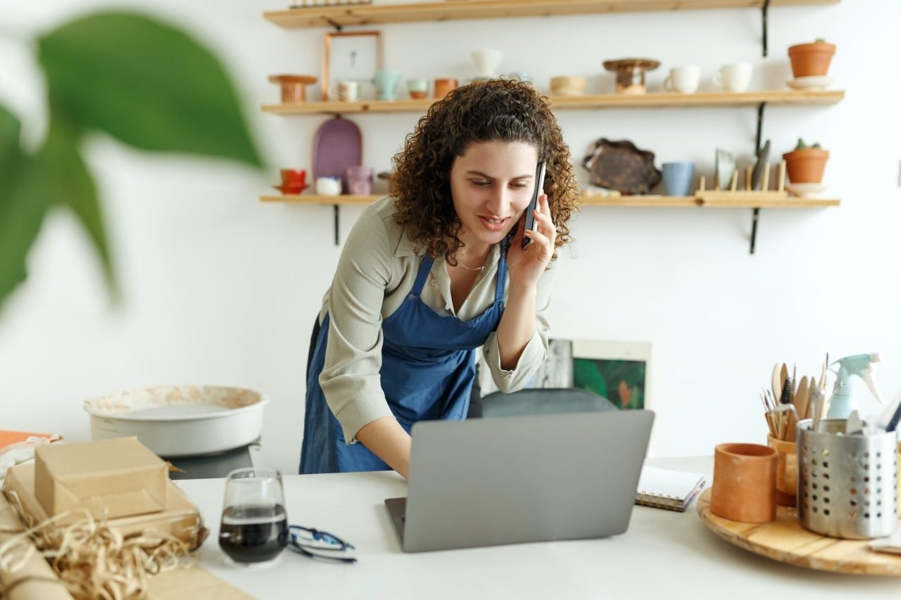 potter entrepreneur using laptop in workshop smiling